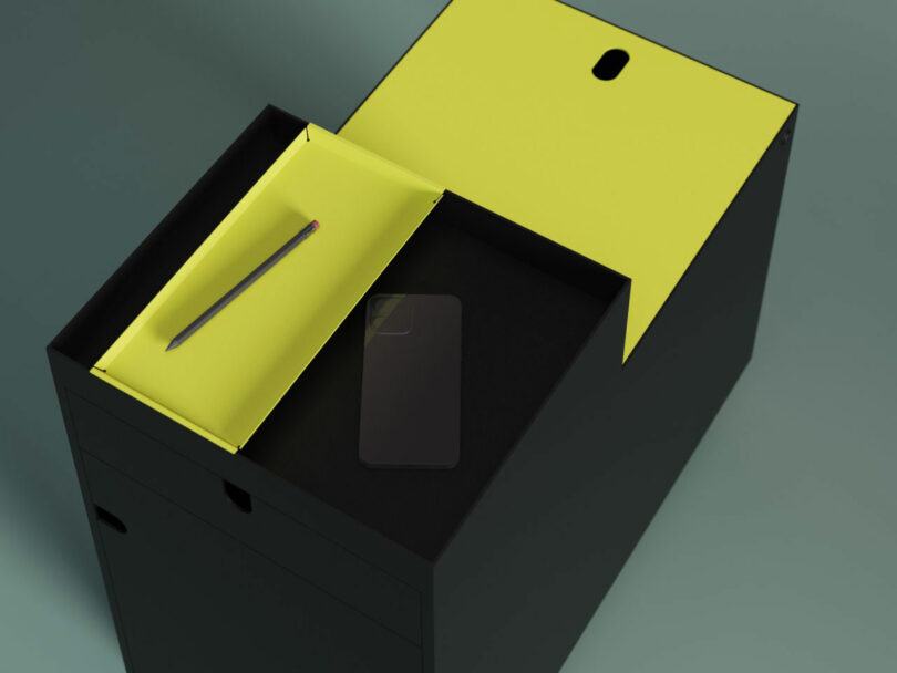 A black desk with a yellow pull-out tray holding a pencil, and a black smartphone resting on the main surface.