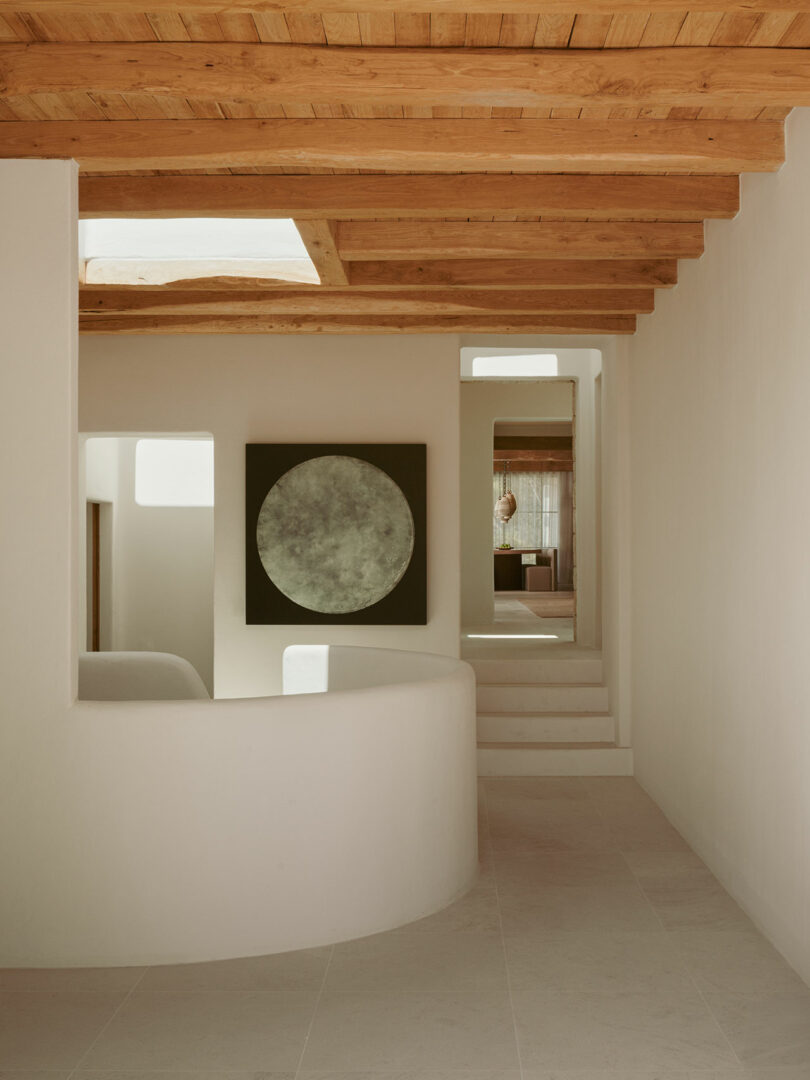 Minimalist interior with smooth white walls, light under the plate, exposed to a wooden ceiling and large circular artworks on the wall near the white stairs.