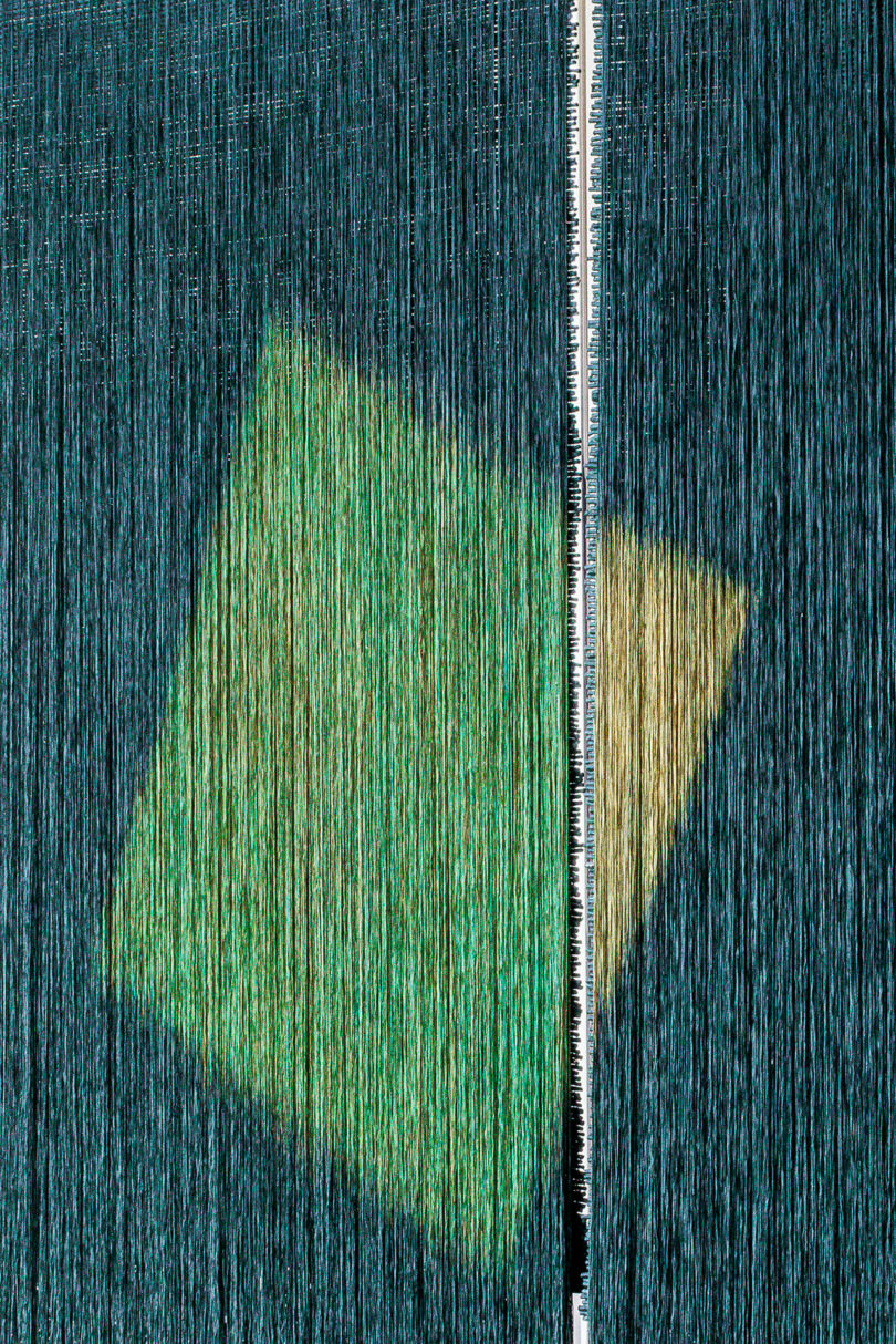 A close-up view of a weaving loom with vertical threads, showing a ruler and a green-yellow geometric shape within the woven fabric, reminiscent of Olga de Amaral's intricate textile artistry.