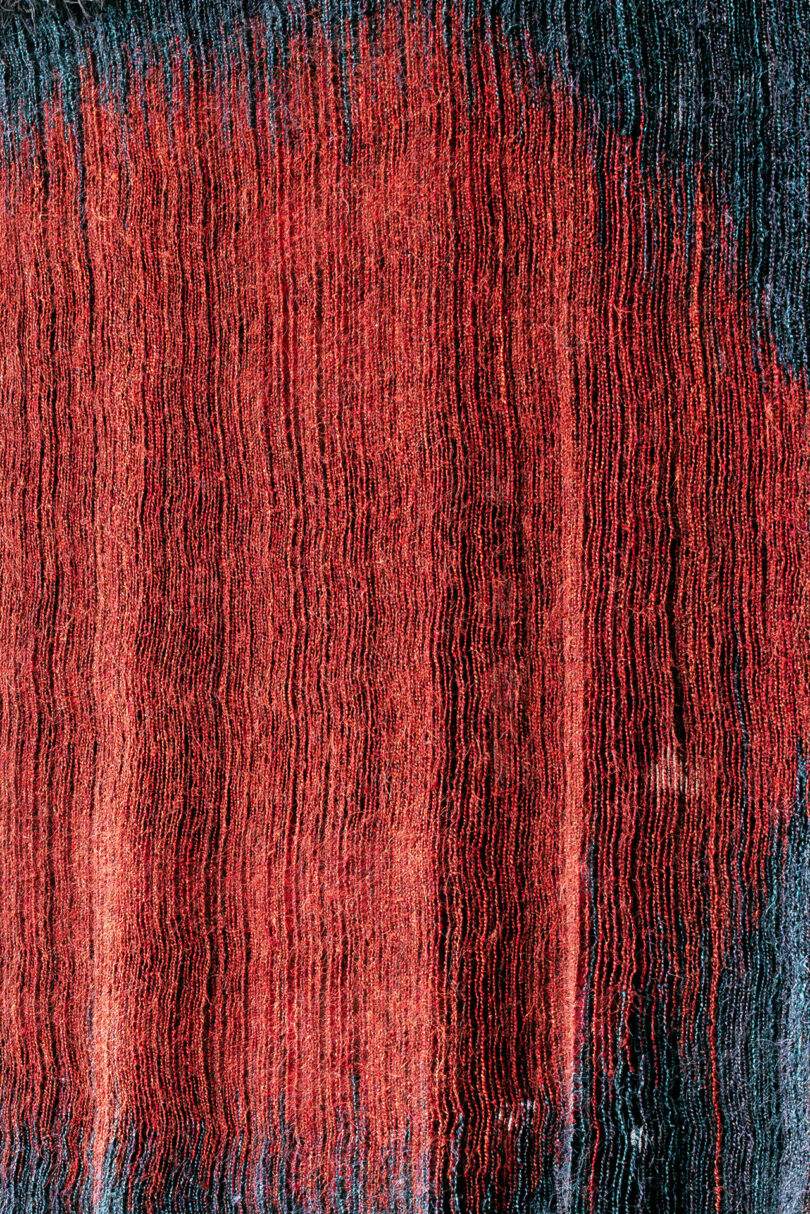 Vertical lines in shades of red and black create an abstract pattern, reminiscent of Olga de Amaral's textured fabric works or painted streaks running from top to bottom.