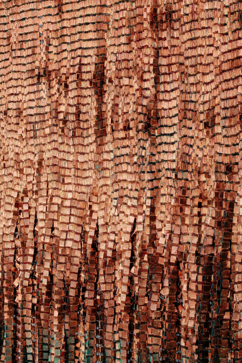 Stacked reddish-brown bricks are arranged in uneven vertical piles, creating a textured wall with varying heights and visible gaps—evoking the intricate, layered compositions seen in Olga de Amaral’s works.