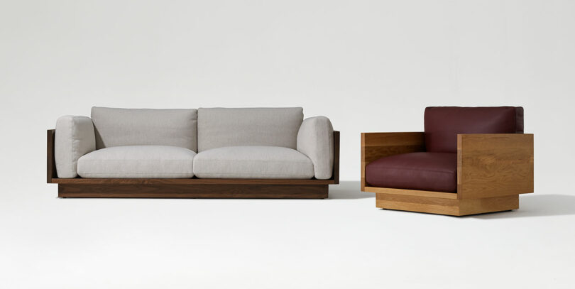 A modern sofa with light gray cushions and wooden frame next to a matching wooden armchair with burgundy cushions, set against a plain white background