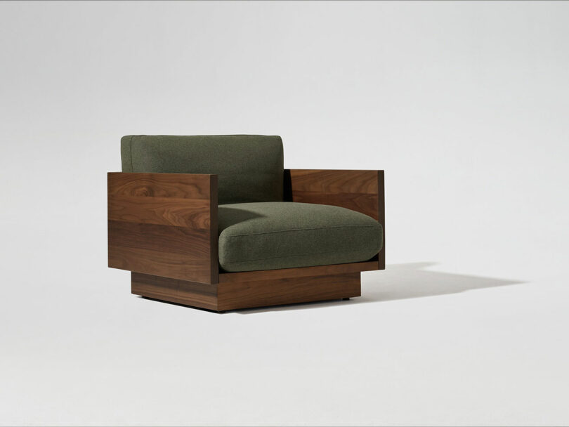 A modern armchair with dark wooden sides and base, featuring olive green upholstered cushions, set against a plain white background