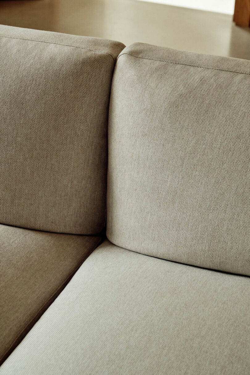 Close-up of the corner where two beige upholstered sofa cushions meet on a fabric couch