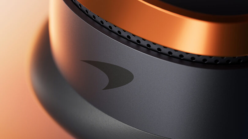 Close-up of a metallic cylindrical object with an orange and black color scheme, featuring a stylized logo and small perforations near the top edge.