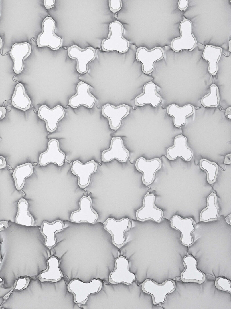 A pattern of repeating, three-pronged, white geometric shapes with raised edges, set against a light gray background.