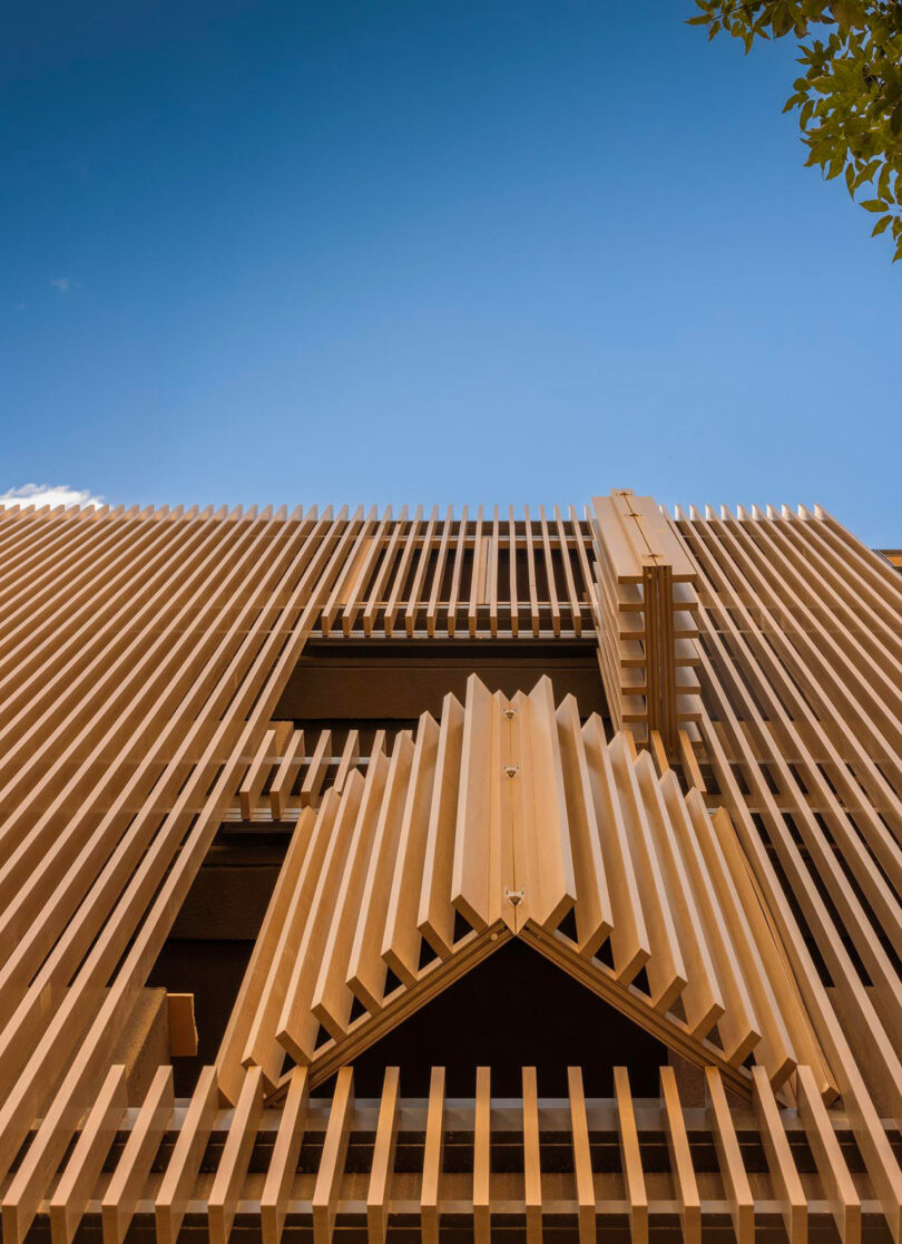 Close-up view of a modern building facade with vertical wooden slats and adjustable folding panels against a clear blue sky.