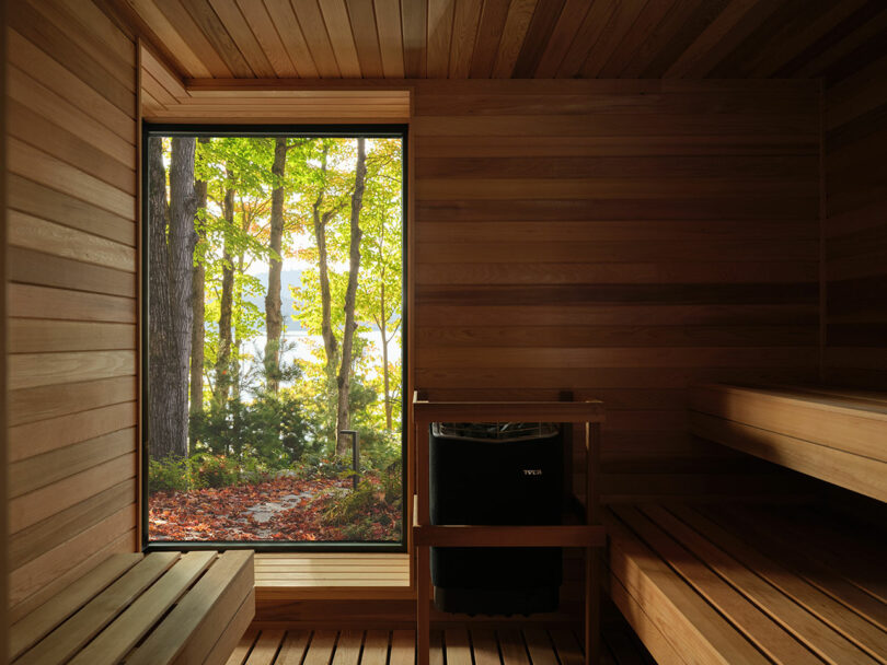 Interior of a wooden sauna with a large window offering a view of trees and a lake outside.
