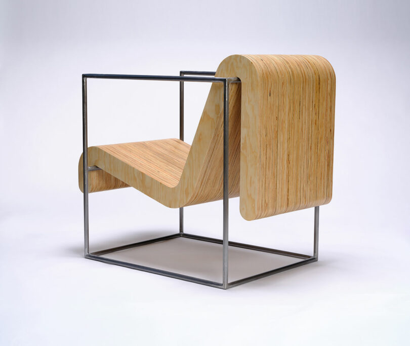 A modern chair with a curved, layered plywood seat and backrest, supported by a minimalist metal cube frame, set against a plain white background.