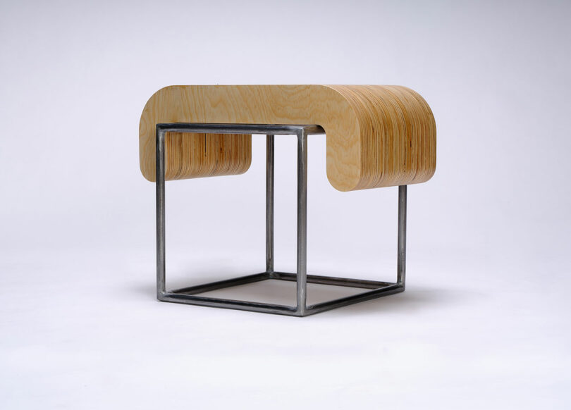 A modern stool with a curved plywood seat resting on a square metal frame, set against a plain white background.