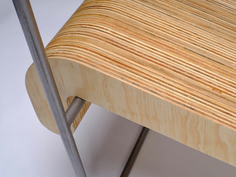 Close-up of a wooden bench seat with visible layered plywood and metal legs, showcasing the curved edge and construction details.