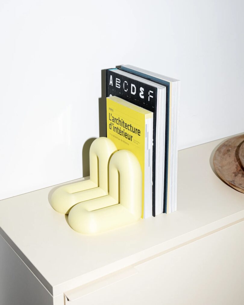 A set of books supported by two pale yellow, rounded bookends on a light-colored cabinet, with a wooden tray partially visible to the right