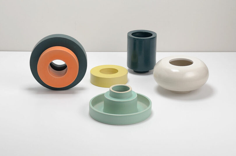 Five components of ceramic vases in different geometric shapes and dimplified colors are regulated on a white surface against a regular white background