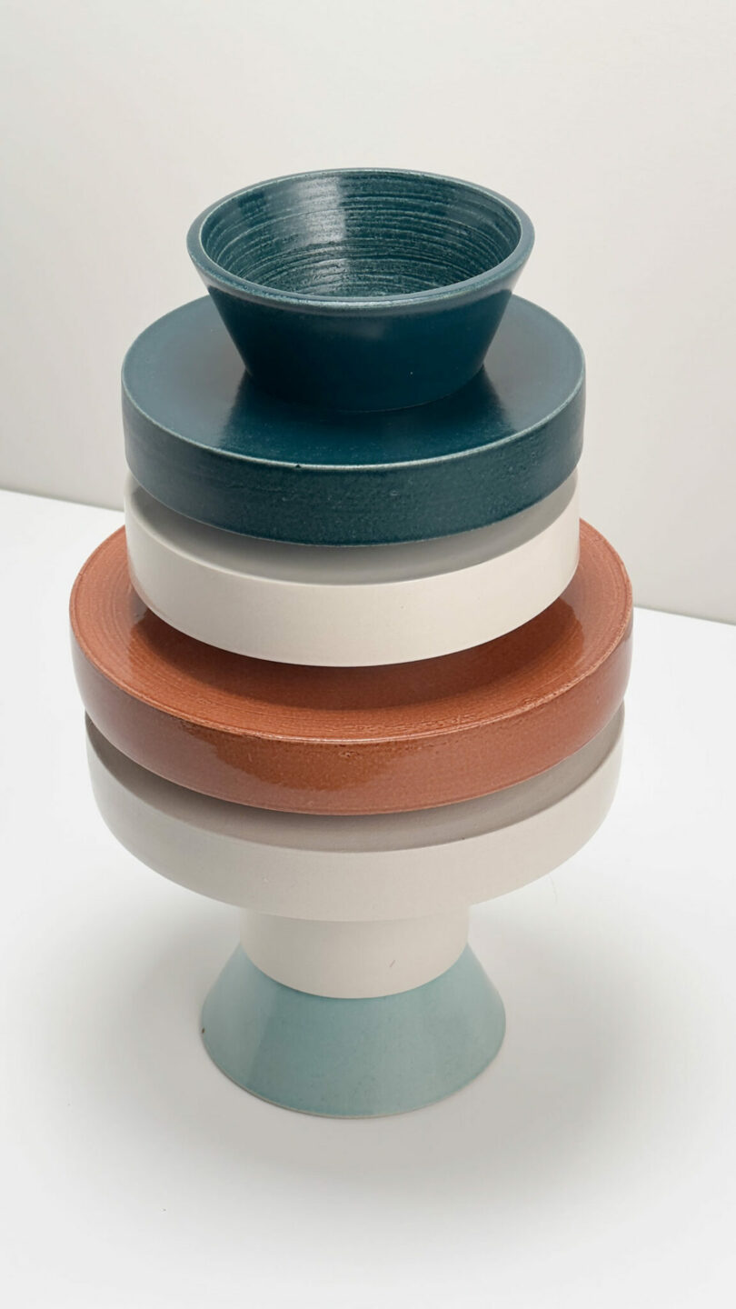 Freedom of five ceramic components of different sizes and colors is balanced vertically on a white surface from a regular background.