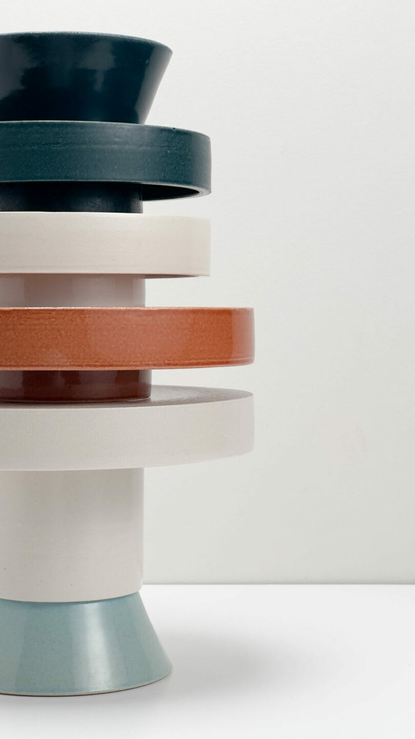 Freedom of five ceramic components of different sizes and colors is balanced vertically on a white surface from a regular background.