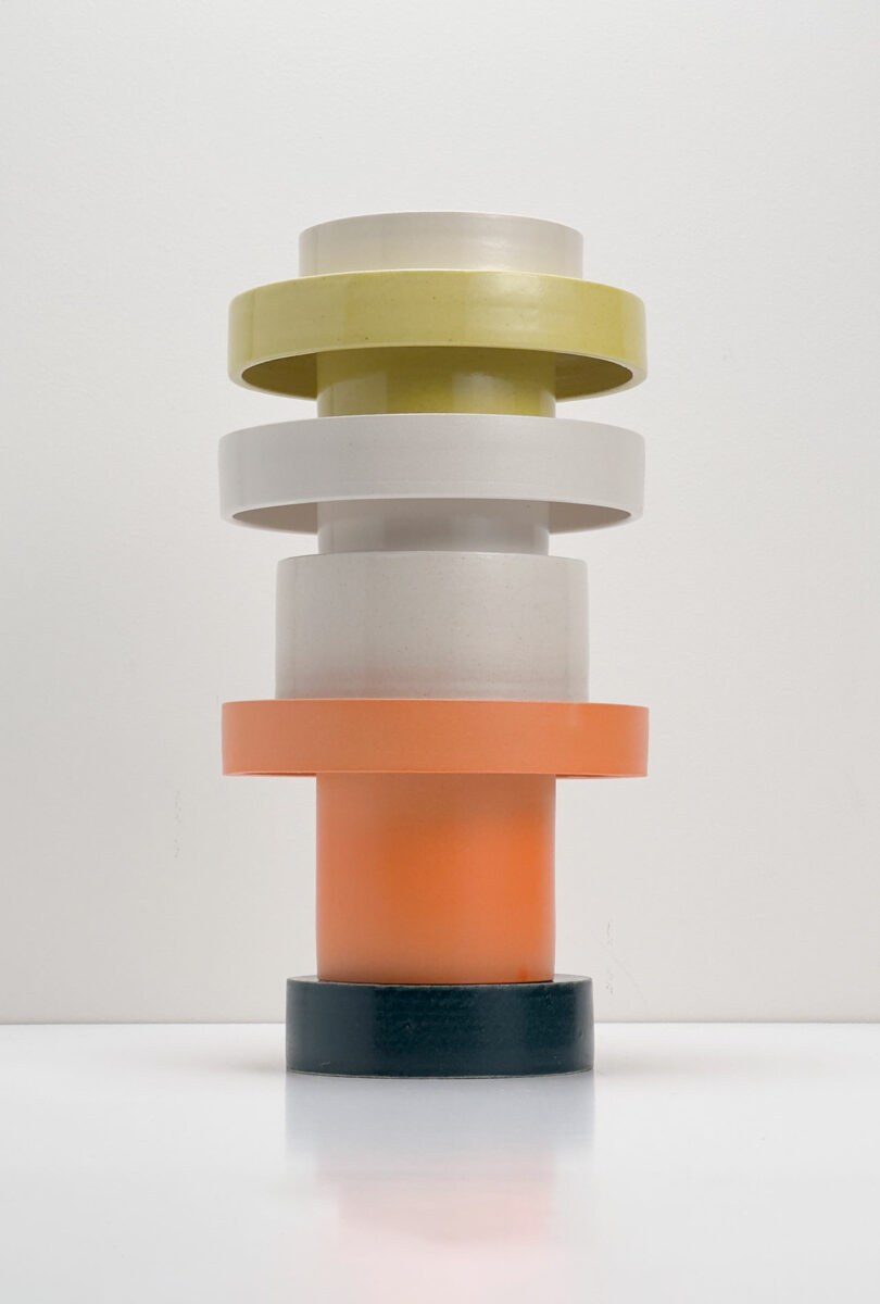 Vertical bundle of components of cylindrical vases in blue, orange, white, yellow and cream colors against ordinary white backgrounds.