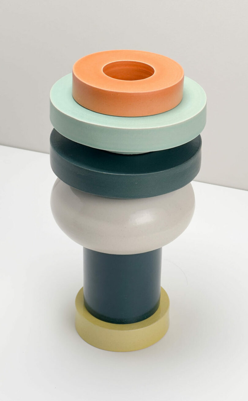 A minimalist vase composed of complex, colorful geometric shapes, including cylinders and a rounded shape, placed on an ordinary white background.