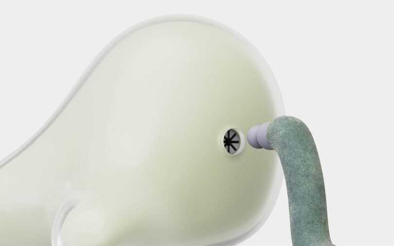 A close-up view of a gray and greenish earbud being inserted into the charging port of a white charging case.
