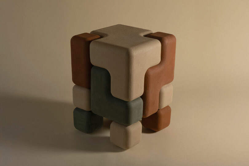 A geometric, interlocking sculpture by Winkle Ceramic Design, made of smooth, blocky shapes in earth tones and arranged to form a distinctive cube-like structure.