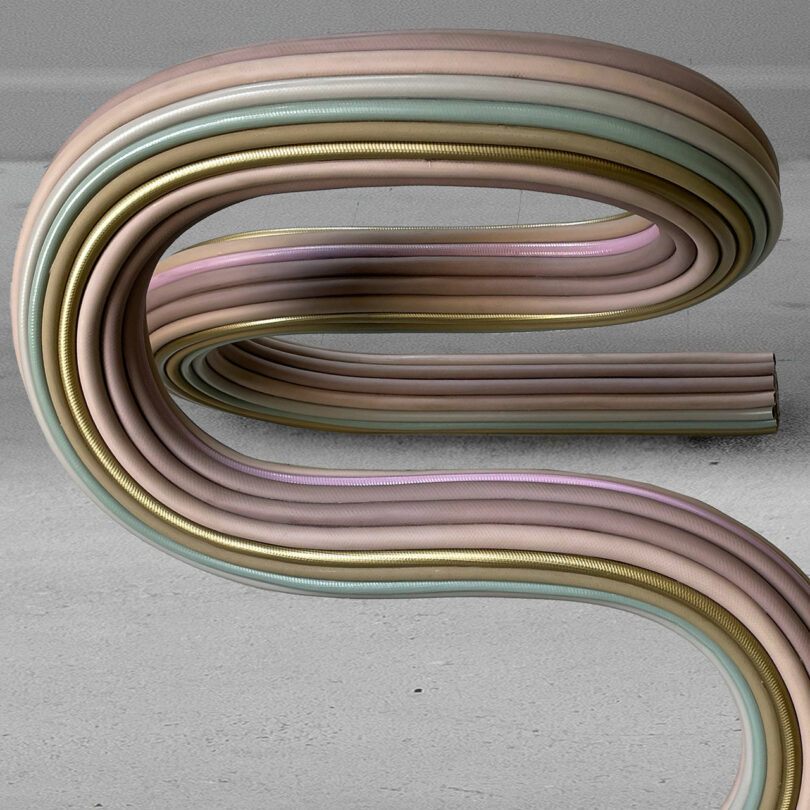 Curved, overlapping pastel-colored hoses or tubes by Ara Thorose rest on a gray concrete surface with a light gray wall in the background.