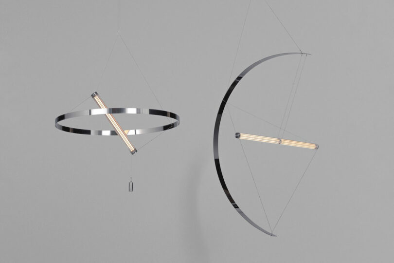 Two modern FANZI pendant lights with metallic circular and semi-circular frames, each suspending a horizontal tubular bulb, hang against a plain gray background.