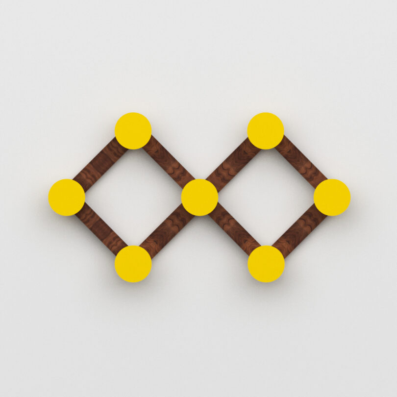 A geometric wall hook of two connected diamonds formed by brown wooden sticks with yellow circles at each corner on a white background.