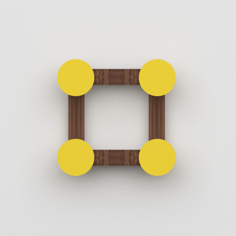 A square wall hook made of brown wooden bars with a yellow circle at each corner, viewed from above on a plain white background