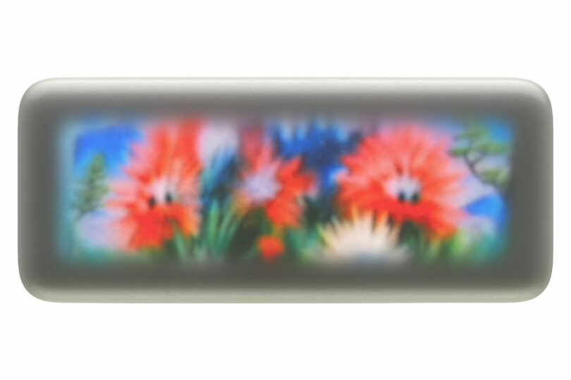A rectangular, gray-framed device displays a blurred image of red and white flowers with green stems against a blue background.