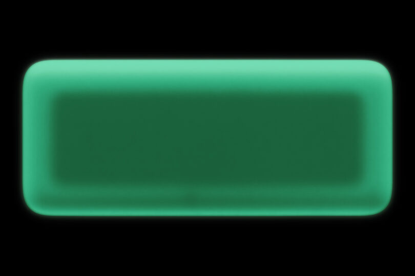 A rectangular, glow-in-the-dark device with rounded corners, viewed against a black background.