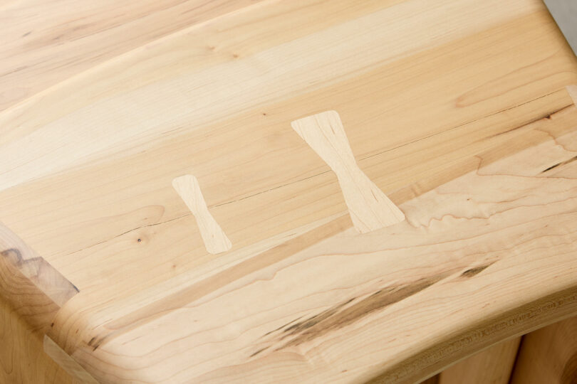 Close-up of a light-colored wooden surface with two butterfly-shaped inlays of different sizes used to join and stabilize the wood