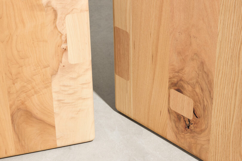 Two wooden boards with visible grain patterns and rectangular patches stand upright on a light, smooth surface