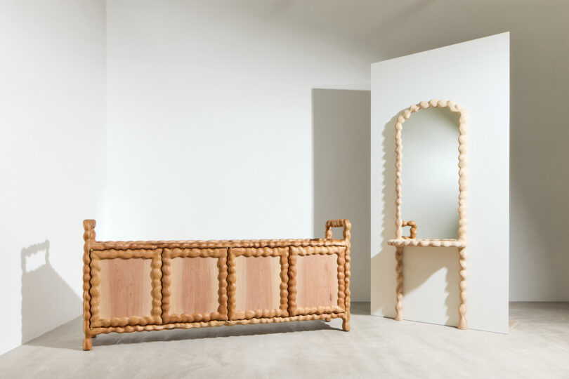 A wooden sideboard and matching mirror with a twisted rope-like frame are displayed against a white wall in a minimal studio setting