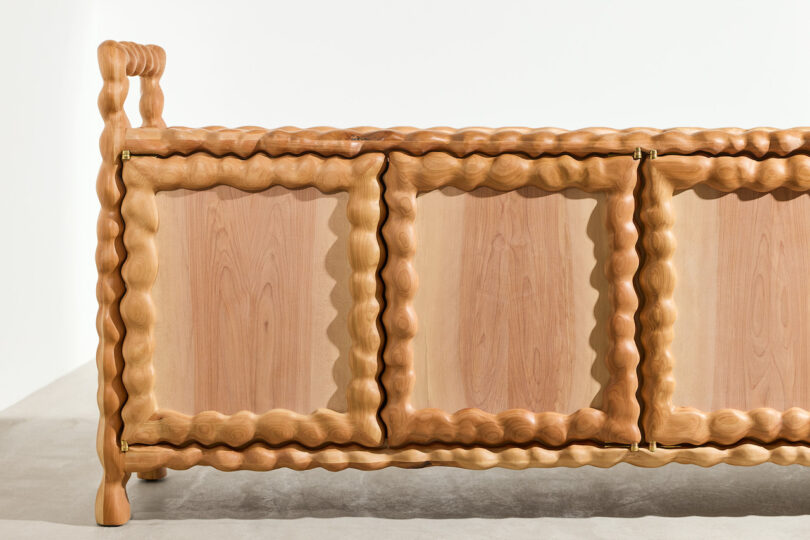 A wooden cabinet with three doors, featuring wavy, sculpted edges and rounded legs, set against a plain background
