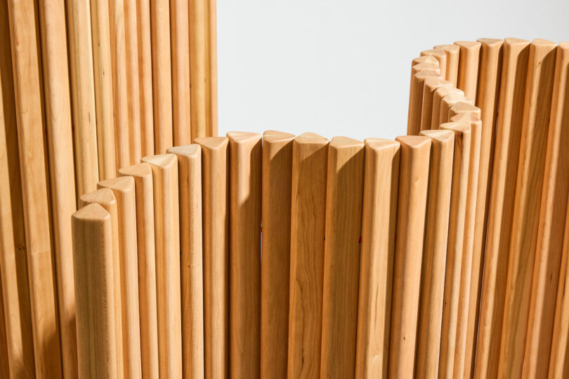 Close-up of vertically arranged, smooth wooden slats forming a wavy, undulating pattern against a plain white background