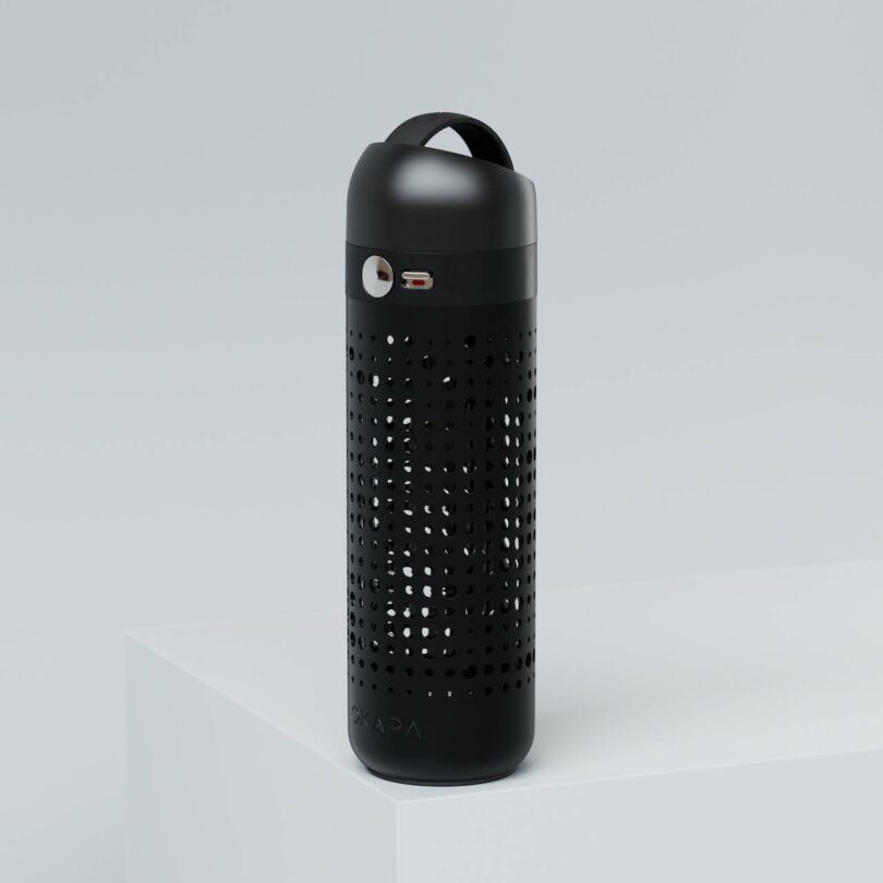 A black cylindrical reusable water bottle with a perforated design and a metal cap, standing upright on a white surface against a light gray background