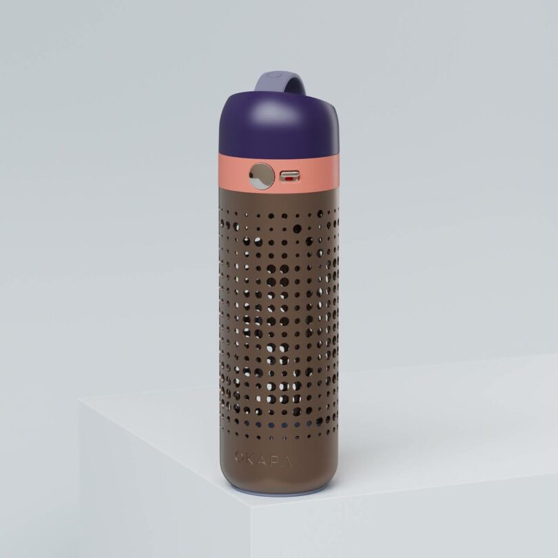A brown and purple water bottle with a perforated design and a pink stripe near the lid, placed on a white surface against a light gray background