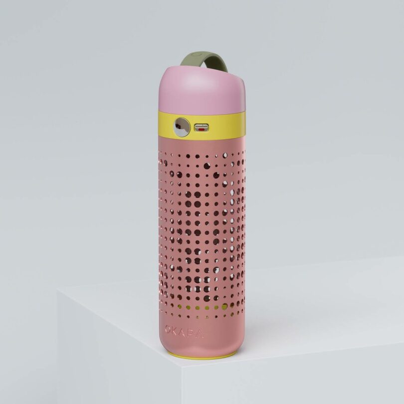 A pink and yellow insulated bottle with a perforated design, a green handle, and a USB port, placed on a white surface against a light grey background
