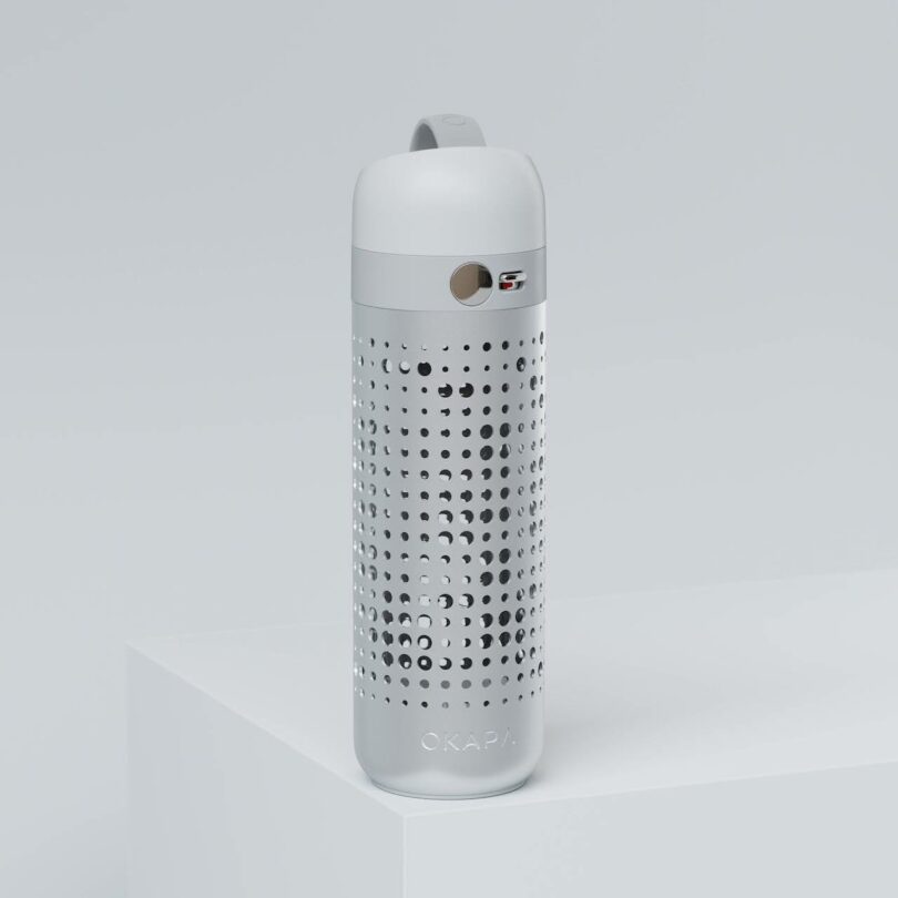 A white and silver reusable water bottle with a perforated design, a round viewing window, and a grey cap sits on a white surface against a light background