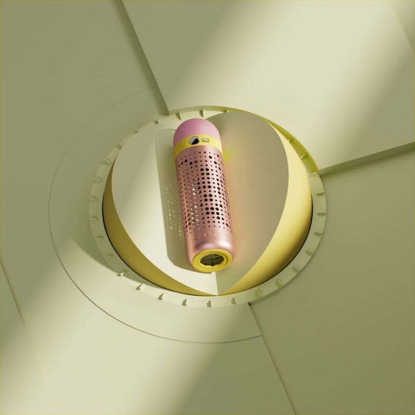 A cylindrical pink and yellow device with perforations is positioned upright in the center of a circular, pale yellow geometric background