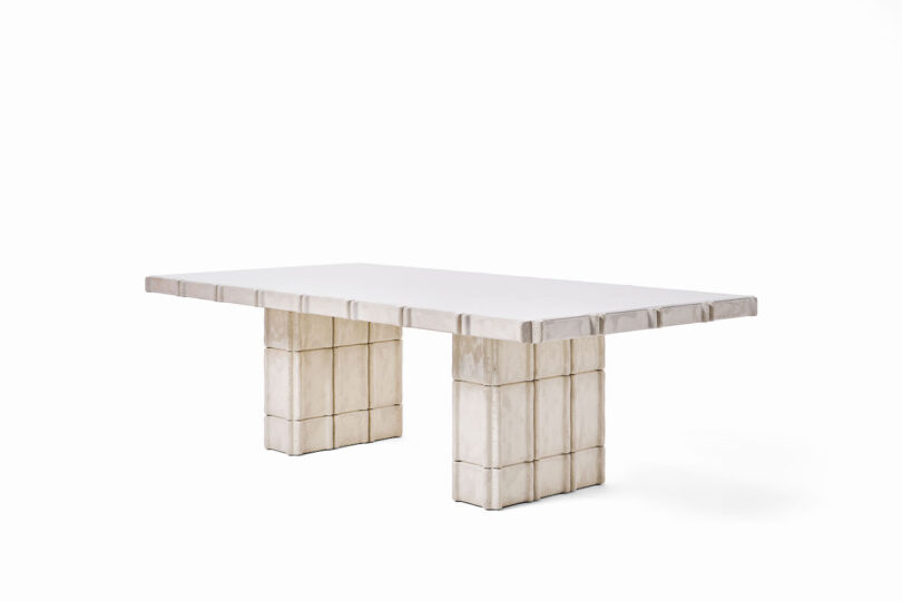 Rectangular table with a thick, light-colored top and two block-style pedestal legs, each made of stacked square segments, set against a plain white background