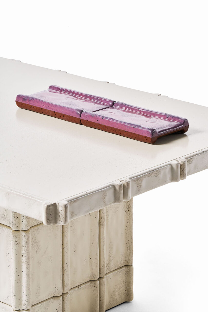 A close-up of a rectangular white textured table with sculpted edges and a set of two rectangular, purple and brown trays placed on top