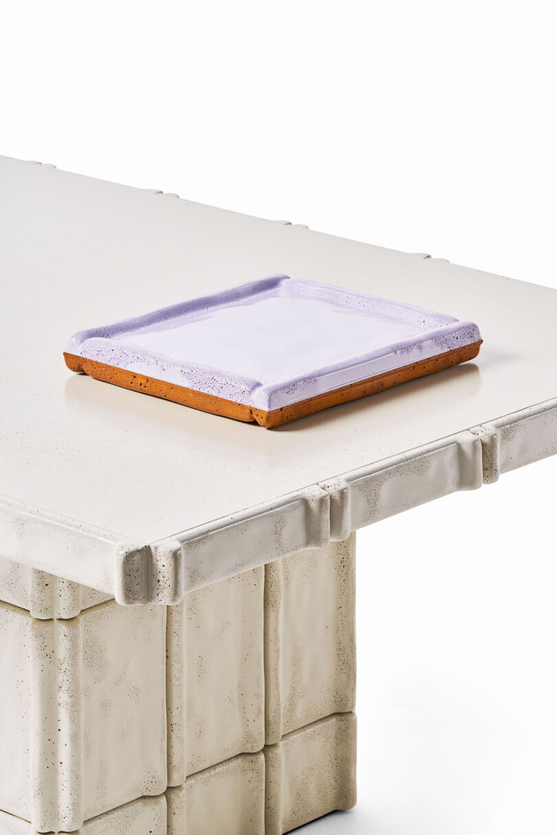 A close-up of a rectangular white textured table with sculpted edges and a set of two rectangular, purple and brown trays placed on top
