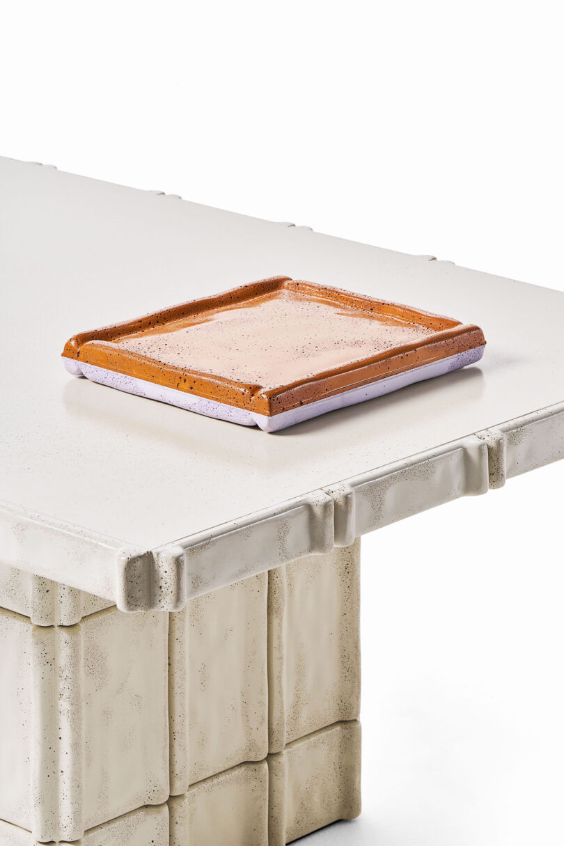 A close-up of a rectangular white textured table with sculpted edges and a set of two rectangular, purple and brown tray placed on top