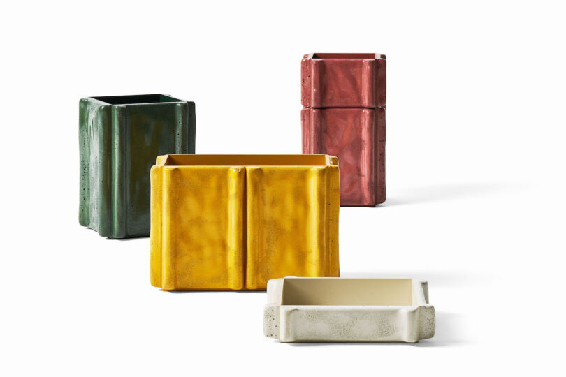 Four rectangular ceramic containers in green, yellow, red, and beige are arranged on a white background; the beige container is lying flat
