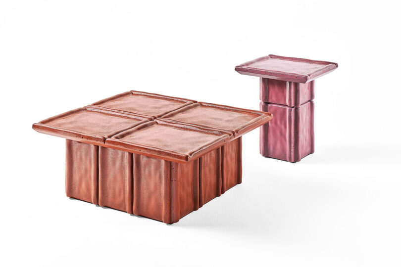 Two tables with square, tile-like tops; one large and rust-colored, the other smaller and pink, both on matching blocky bases, set against a white background