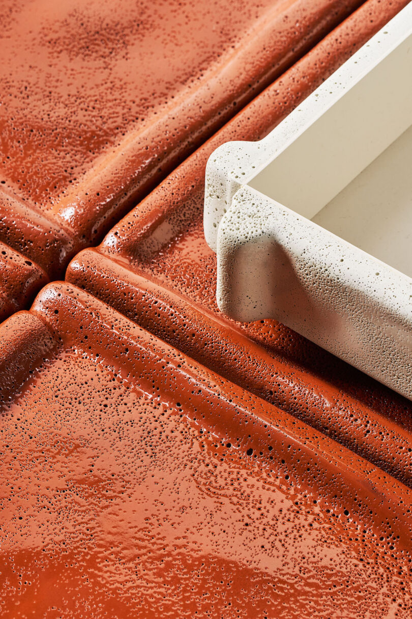 A close-up of textured, glossy terracotta tiles with a white, speckled tray resting on top