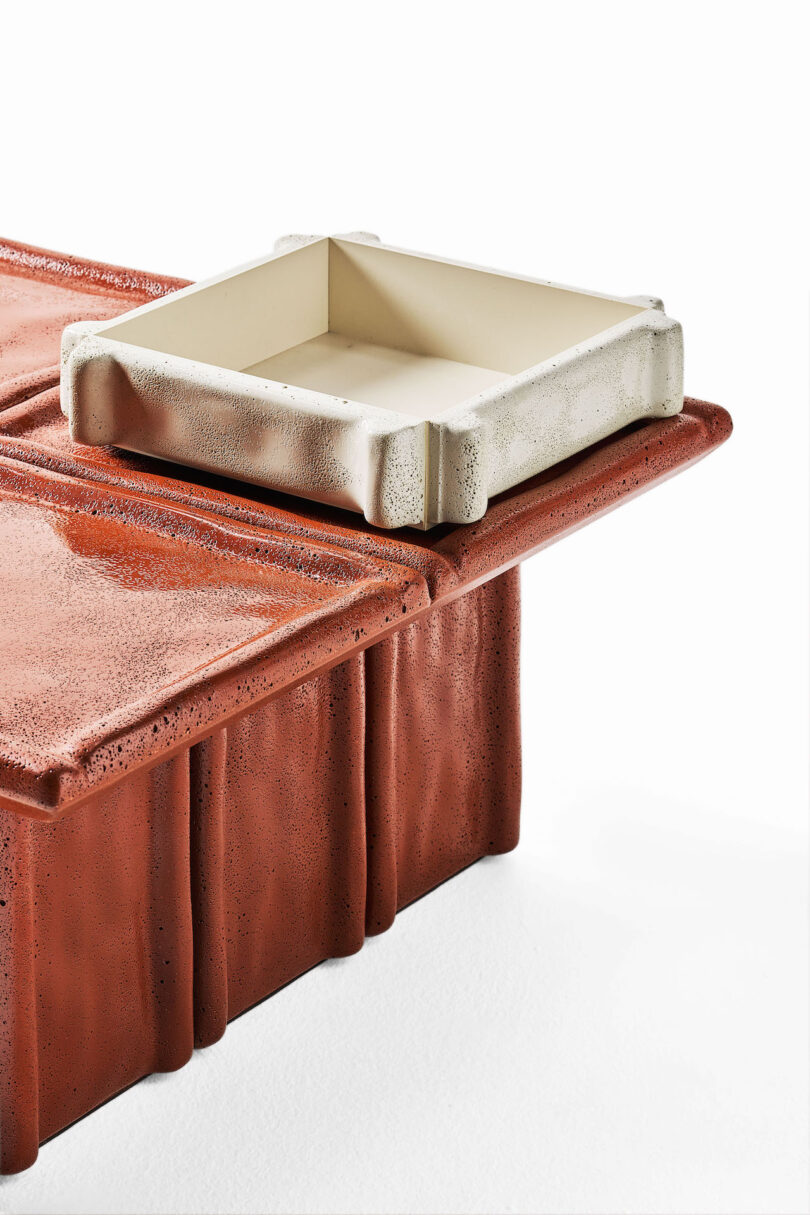 A close-up of a textured, rust-colored table with a square, off-white tray resting on one corner