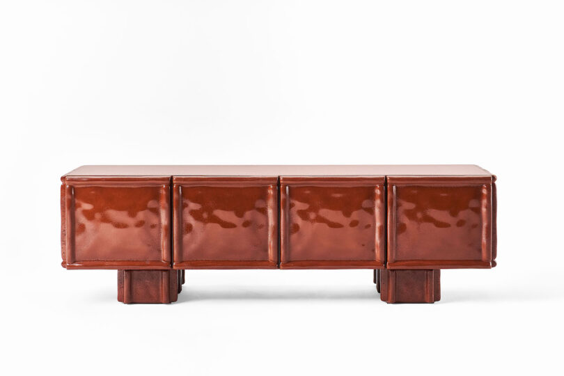 Rectangular brown leather bench or cabinet with four padded panels and short wooden legs, set against a white background