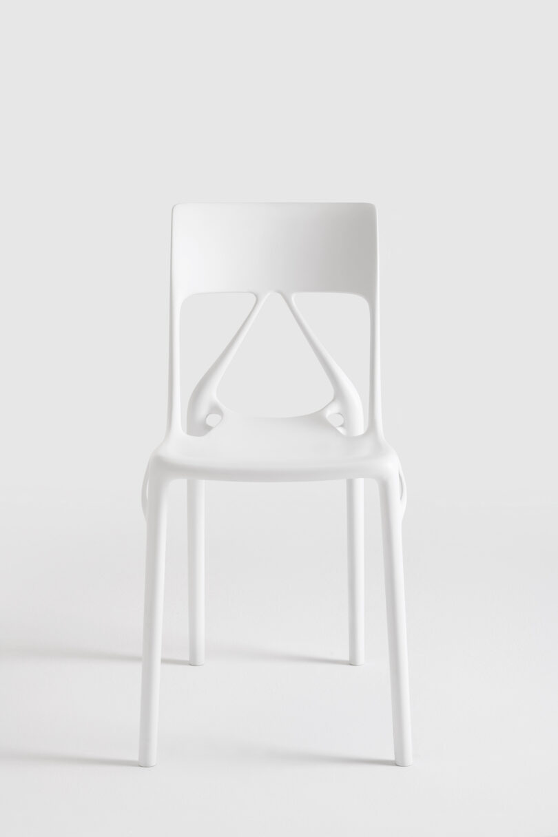 A modern white plastic chair with a curved backrest and cut-out geometric design, placed on a plain white background