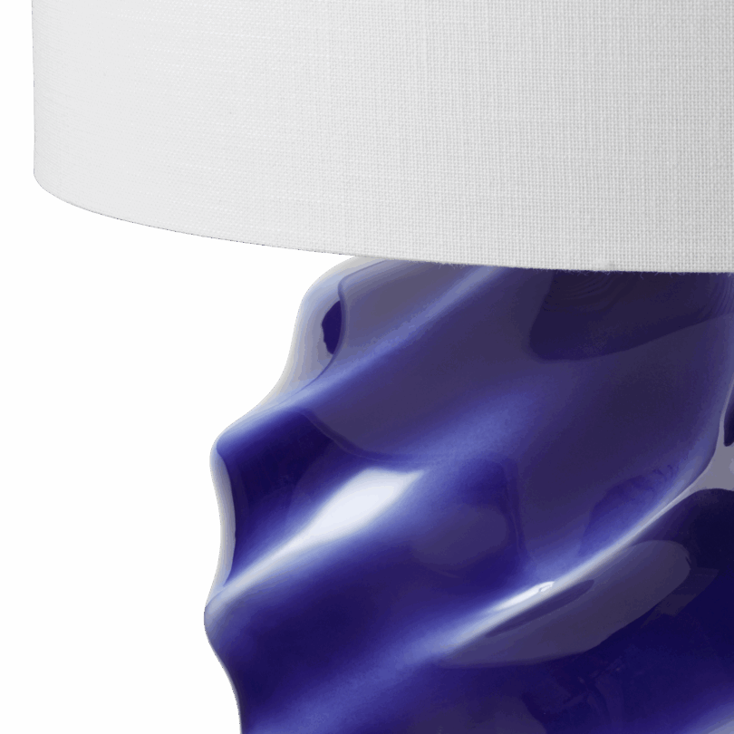 close up of Table lamp with a white cylindrical lampshade and a glossy, wavy, deep blue ceramic base